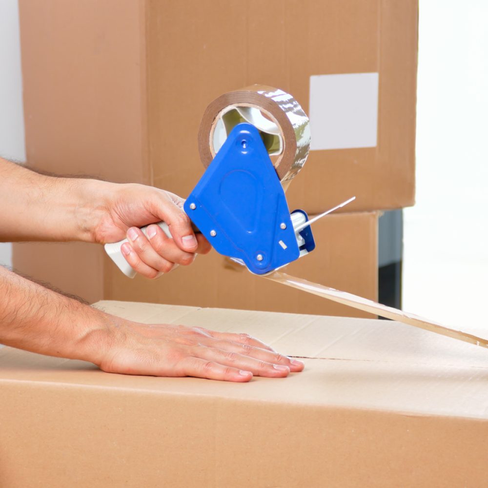 Shot of an unidentifiable young man closing a cardboard box with tape at home